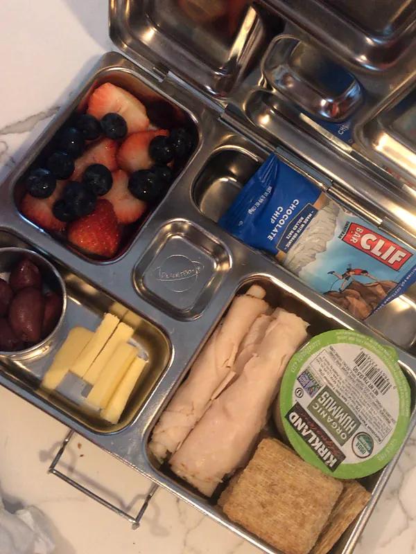 A packed lunch: bento box with berries, cheese, turkey roll-ups, hummus and crackers