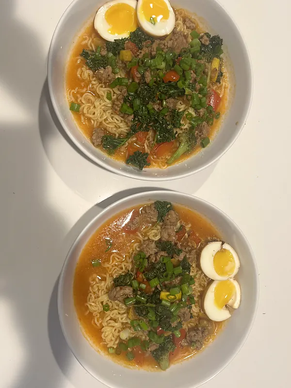Two bowls of ramen with soft-boiled eggs and fresh greens